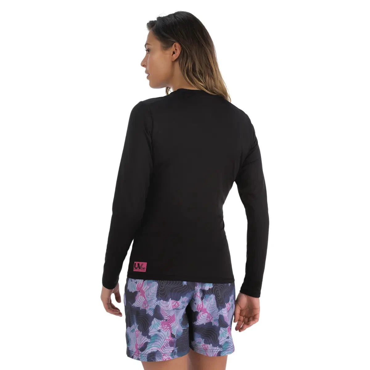 Women's black long-sleeve rashguard riding gear with pink logo tag on hem; purple patterned shorts.