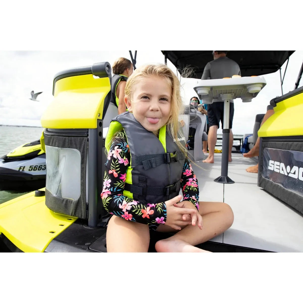 Sea-Doo Kids' Sandsea PFD life jacket in gray with neon lime accents, worn by girl on a boat.